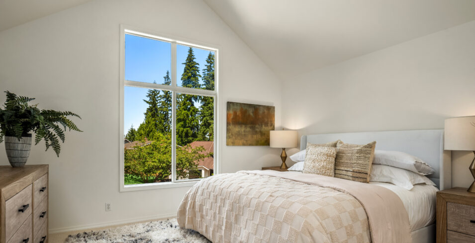 Primary bedroom with vaulted ceiling, new carpet, and large window with treetop view in Kirkland home