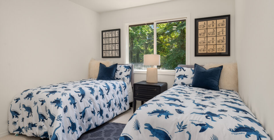 Bedroom staged with twin beds and leafy window view in Kirkland Highlands home for sale