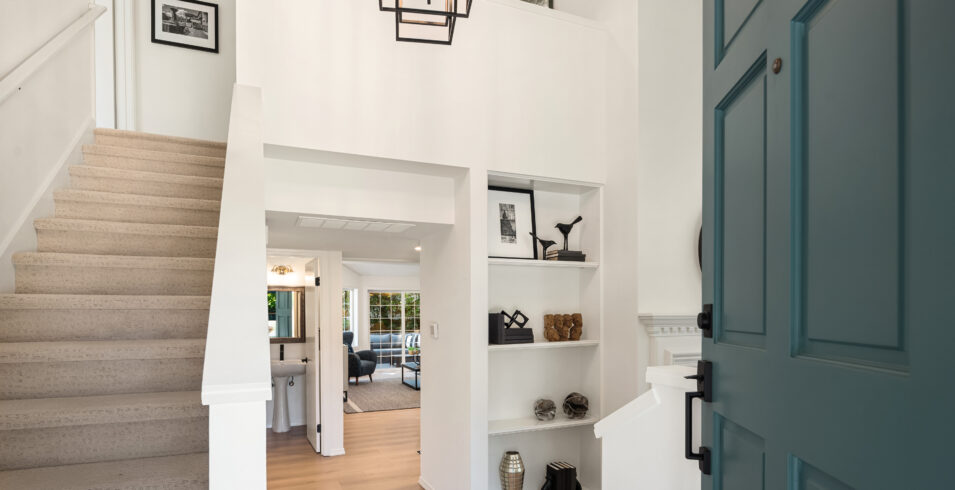 Entry of Kirkland Highlands home with blue green front door, staircase with white risers, and built in shelving