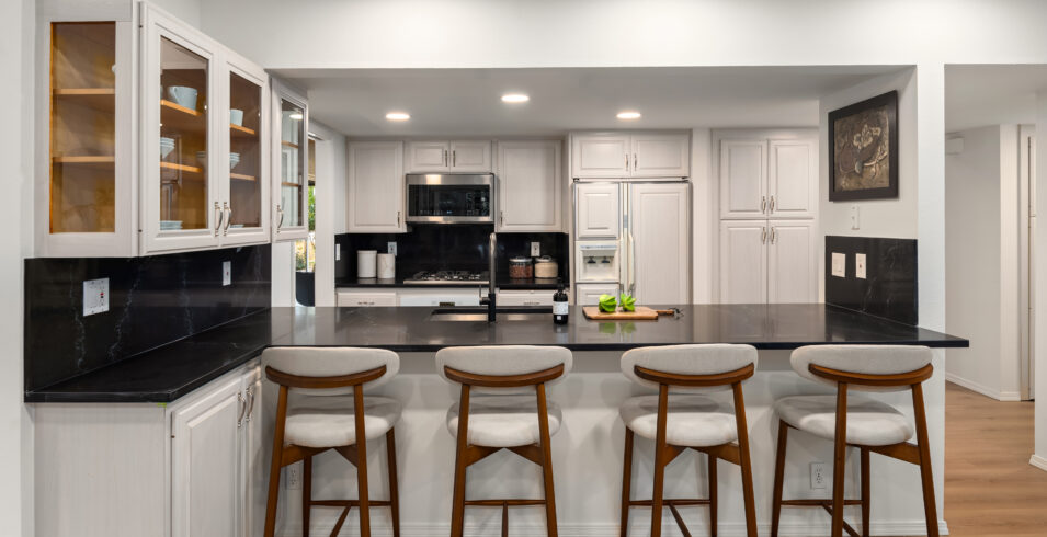 Full kitchen view with white cabinets, glass uppers, black quartz counters, and breakfast bar in Kirkland home