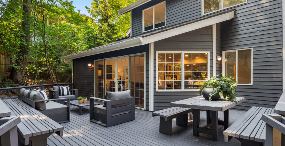 Outdoor dining table and benches on restored deck with window wall behind in Kirkland home
